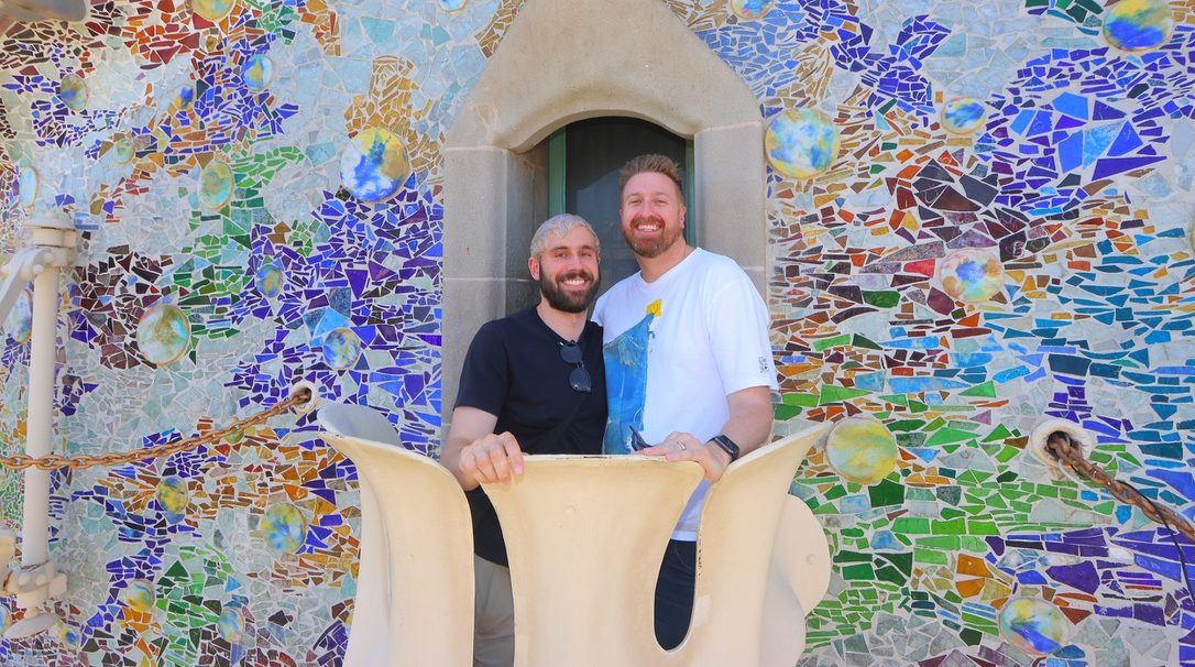 Casey and Trevor standing together in front of a colorful mosaic wall.